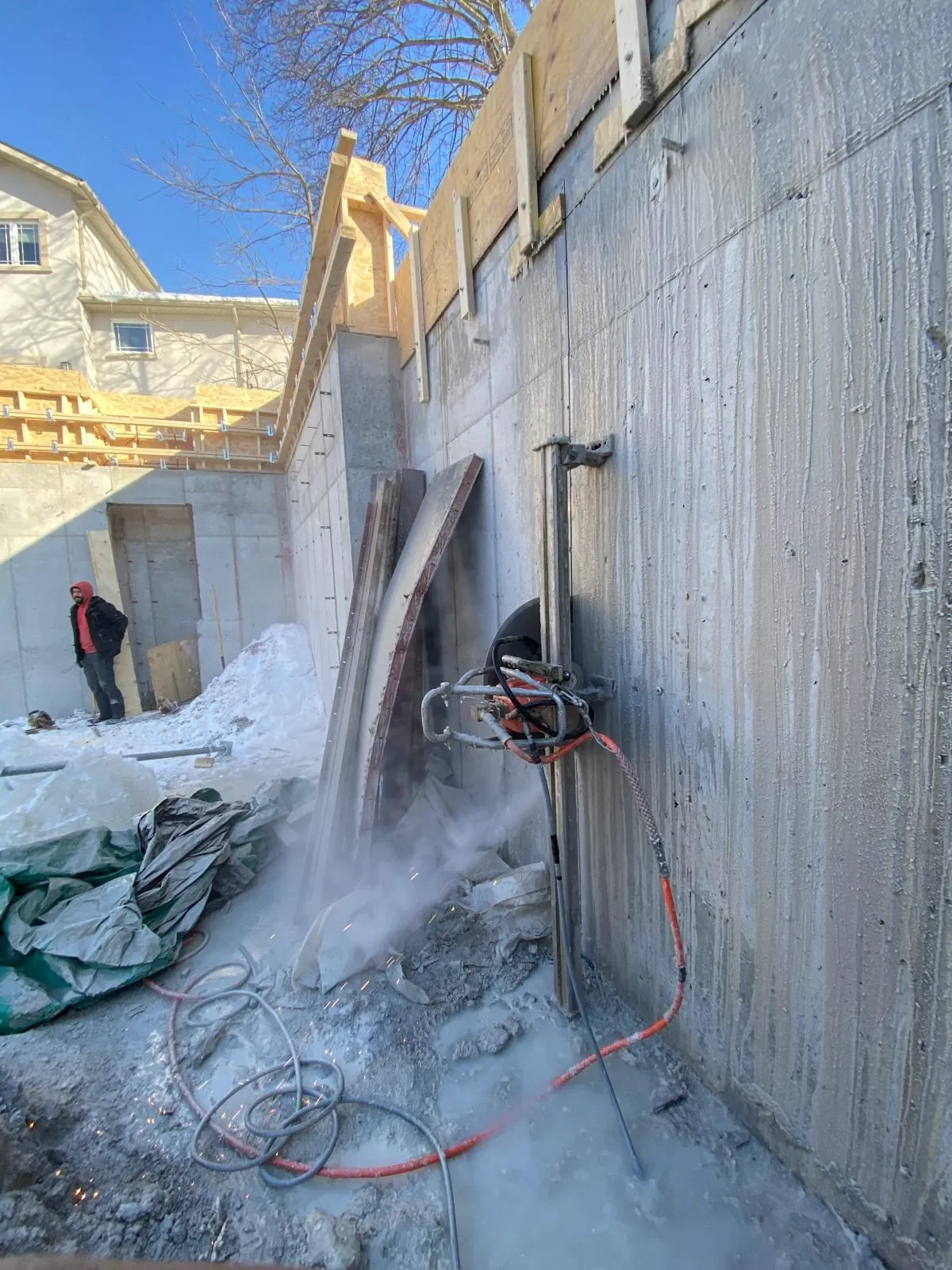 Wall saw cutting a concrete foundation wall on a winter job site — Bluehorse Builds crew